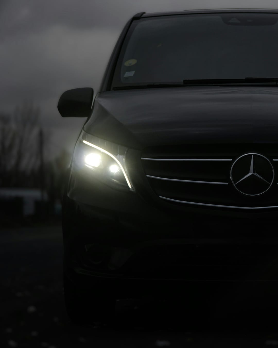 Schwarze Mercedes V-Klasse bei Nacht mit eingeschalteten Scheinwerfern – Premium-Nachttransfer Salzburg